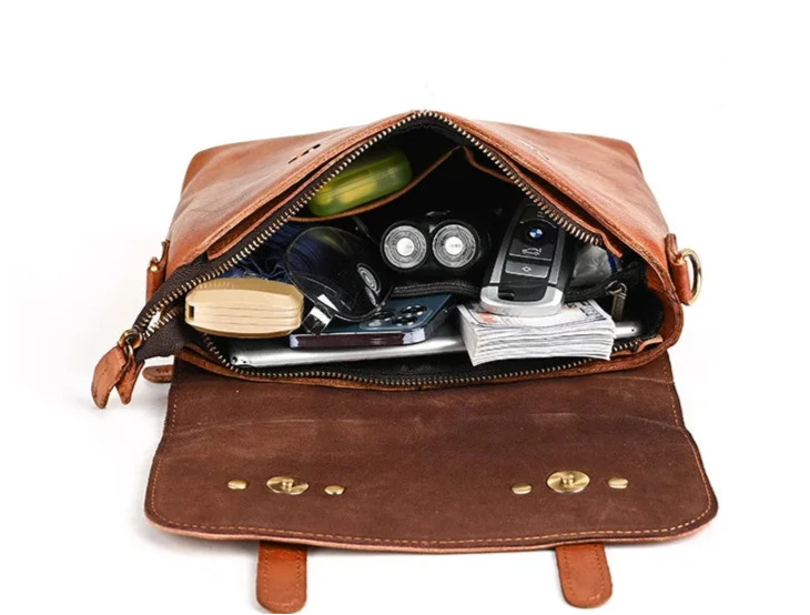 An open brown leather bag showcasing various items inside including a phone, flashlight, and notebook.