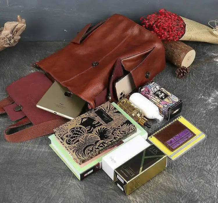A stylish red brown leather backpack surrounded by various items including notebooks, a tablet, and stationery.
