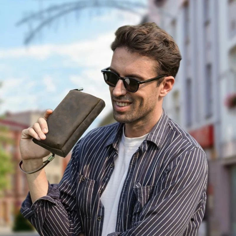 Man holding a leather clutch in an outdoor urban setting.
