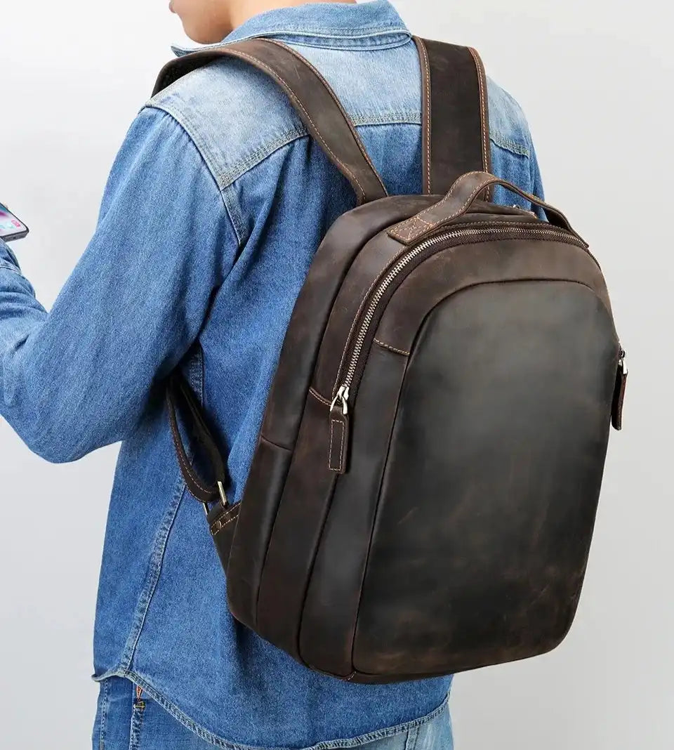 back view of a man in denim shirt wearing a stylish leather backpack, highlighting its modern and durable design.