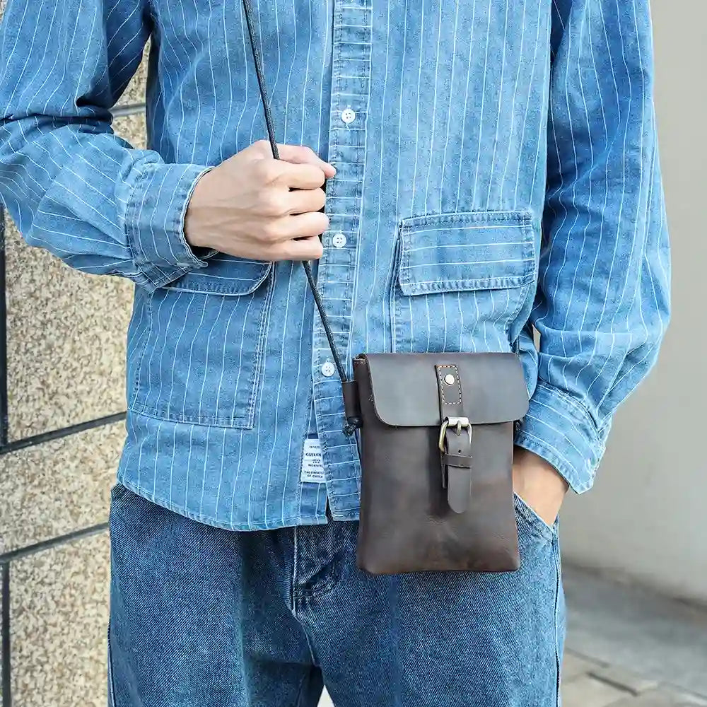 Person wearing a blue denim shirt and holding a brown leather crossbody bag, displaying modern look.