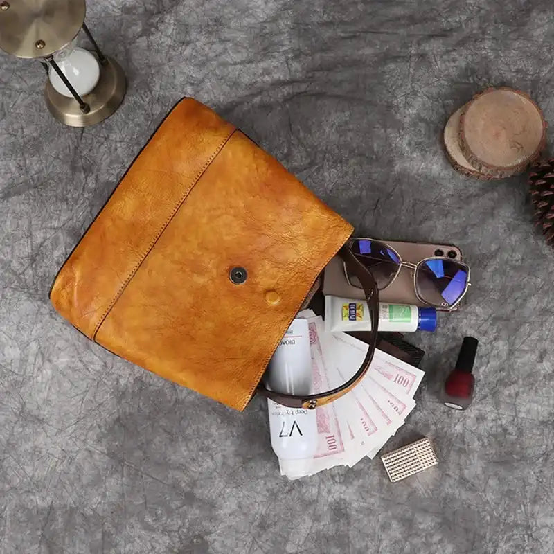 Yellow leather handbag open, displaying assorted items such as sunscreen, sunglasses, nail polish and cell phone.