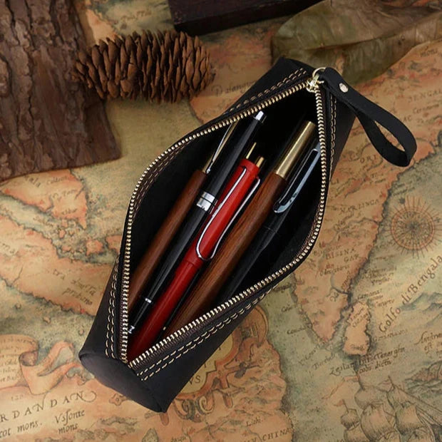 An open zippered black leather pen case showcasing various pens on an antique map.