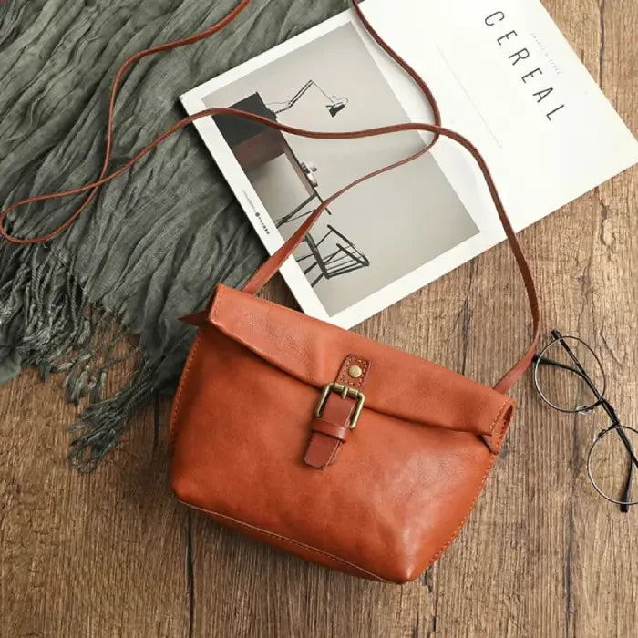 Orange leather crossbody bag with elegant buckle and long strap, top view.