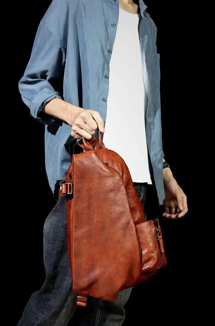 A brown leather shoulder bag with ergonomic design held by a man from handle.