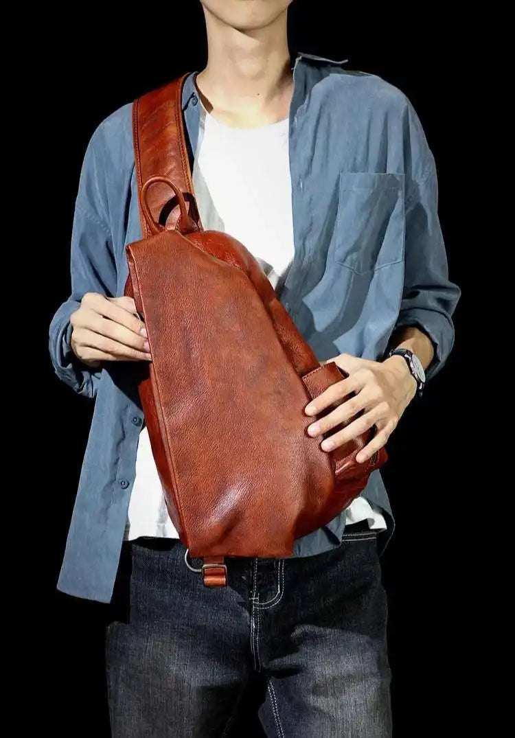 A brown leather shoulder bag with ergonomic design worn by a man on the chest across the body.