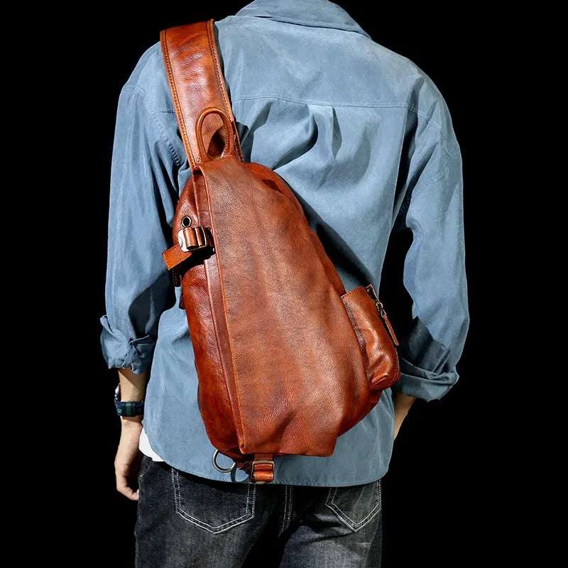A brown leather shoulder bag with ergonomic design worn by a man on the back across the body.