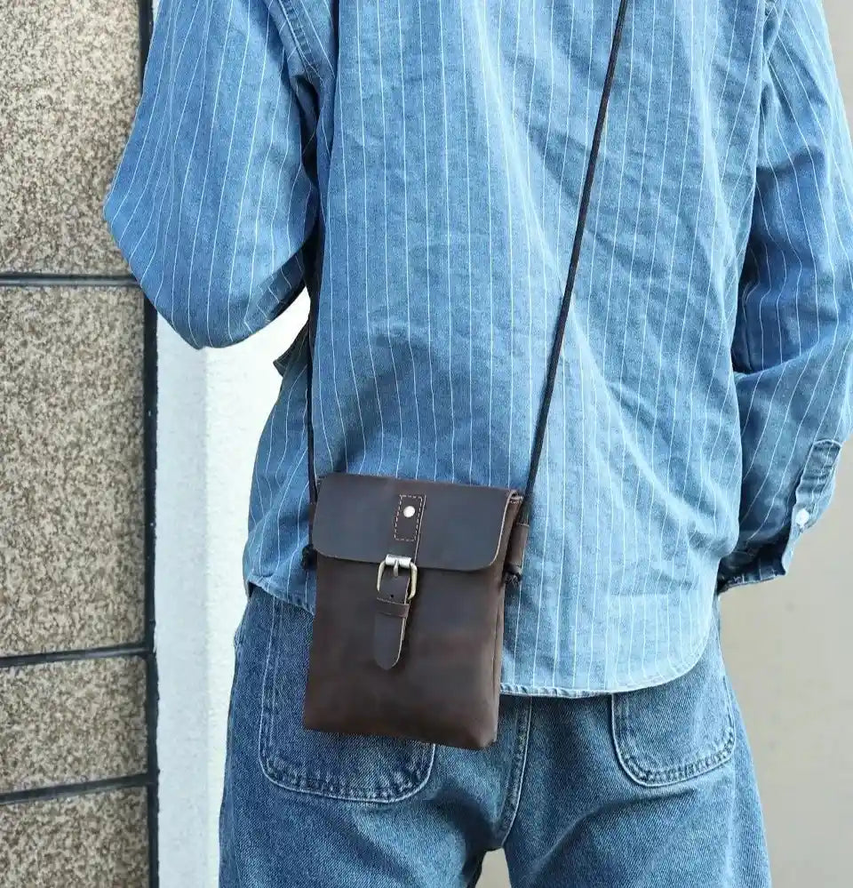 back view of a man wearing a brown leather crossbody bag over a blue shirt. 