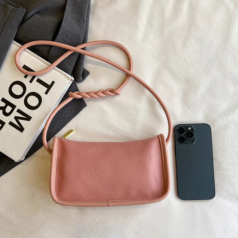 A stylish pink leather crossbody bag resting next to a phone for size comparison.