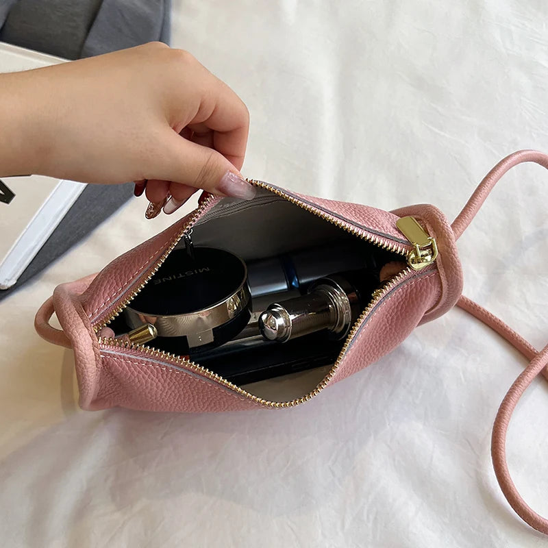 An open pink leather crossbody bag revealing various beauty items inside.