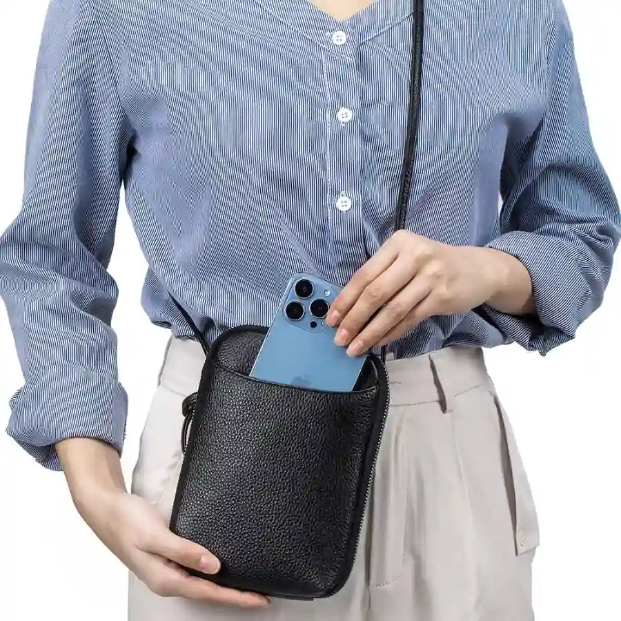 A woman placing her phone into a stylish black leather crossbody bag.