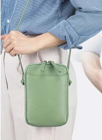 Stylish leather green crossbody bag held by a person - front iew.