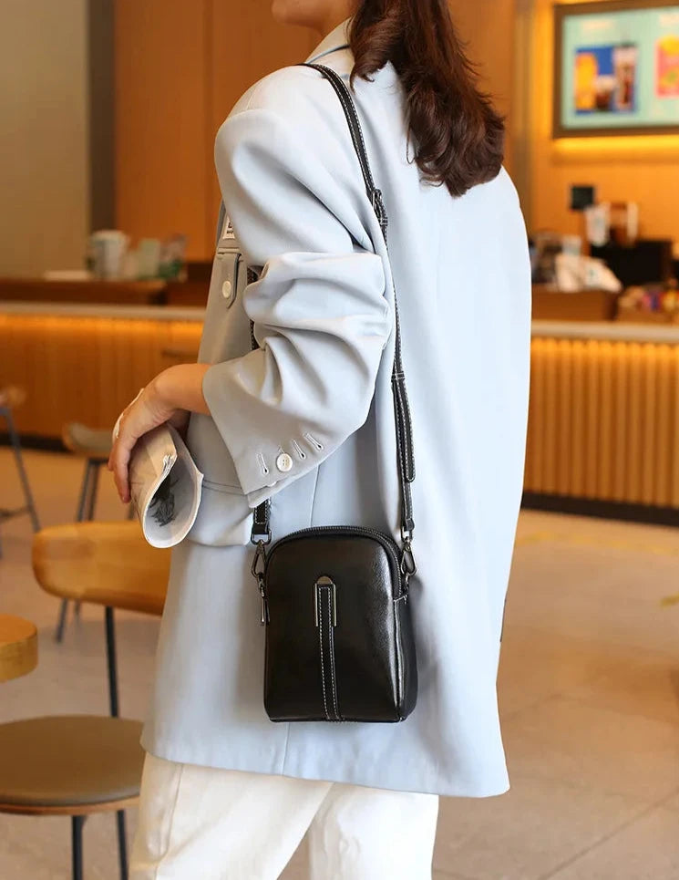 A stylish black leather crossbody bag worn with a light blue blazer in a cafe setting.