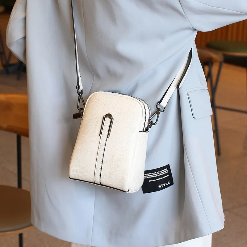 A stylish white leather crossbody bag worn across the body over a light blue outfit.