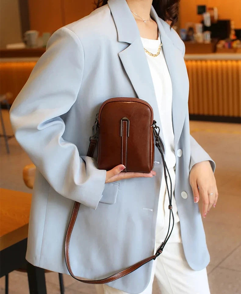 A woman in a light blue blazer holding a stylish coffee color leather crossbody bag in a cafe.