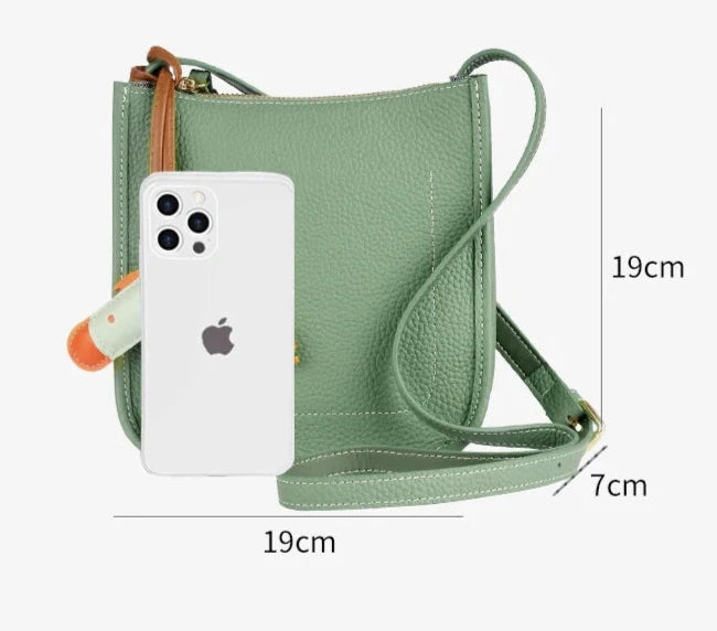 Front view of a stylish green leather crossbody bag with dimensions and smartphone for size reference.
