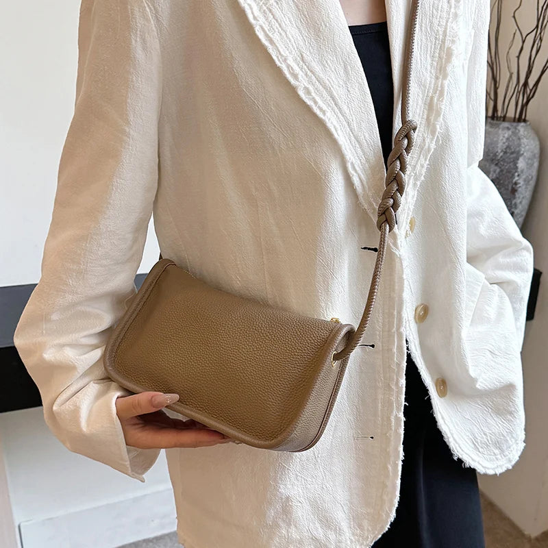 A close-up of a chic khaki leather crossboby with braided strap worn across the body by a woman in a white jacket.