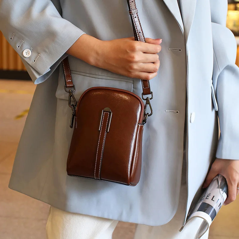 A stylish coffee color leather crossbody bag worn by a person in a light blue blazer.