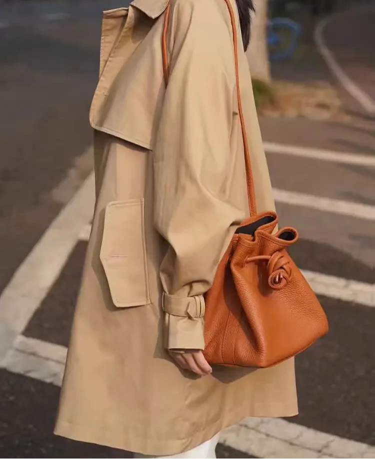 Woman carrying stylish brown leather bag with knot design in a city setting.
