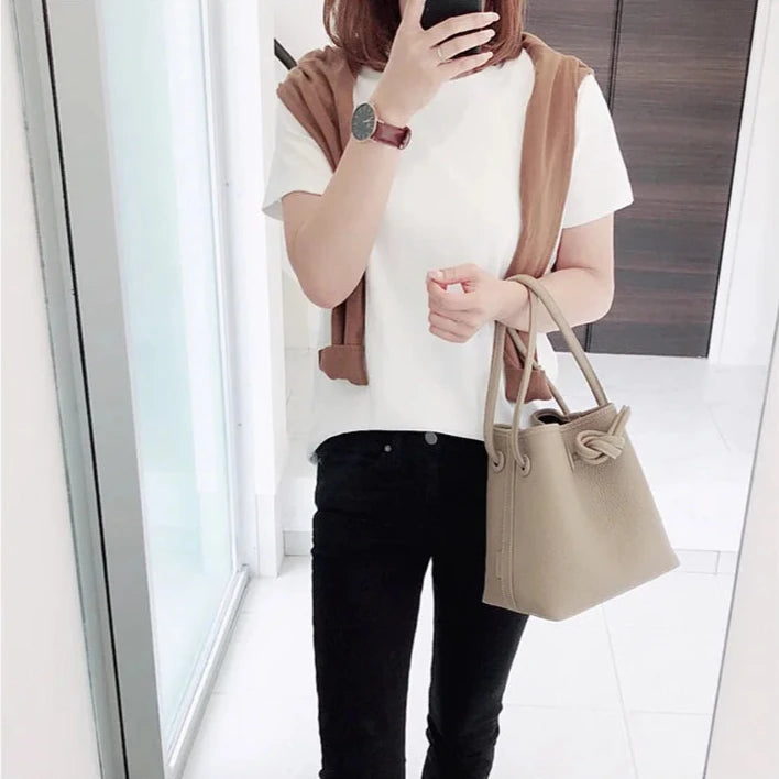 A stylish woman in a white top holding a gray leather handbag showcasing a modern look.