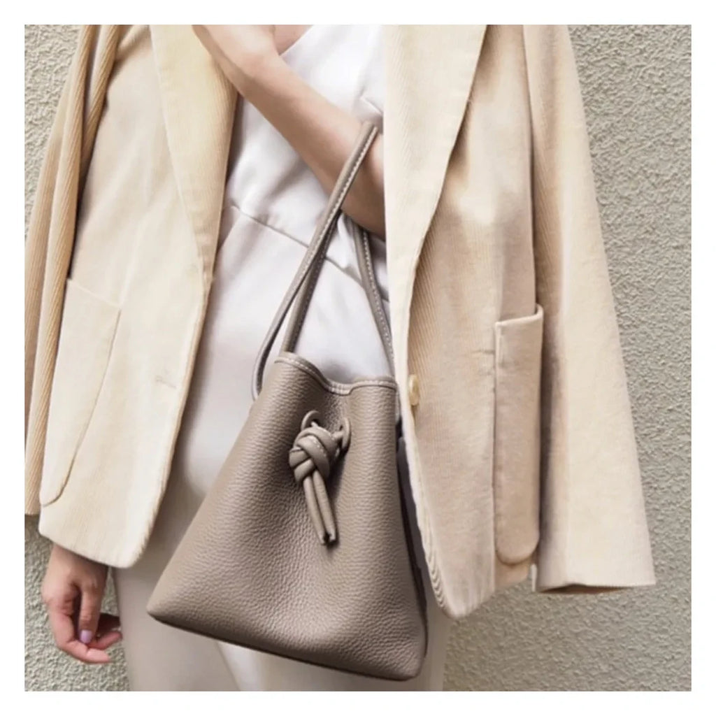 A stylish woman holding an elegant gray leather bucket bag.