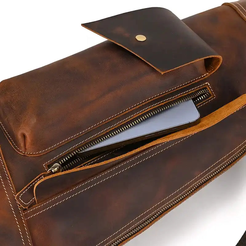 Close-up view of a brown leather  bag with a zipper and a phone inside.