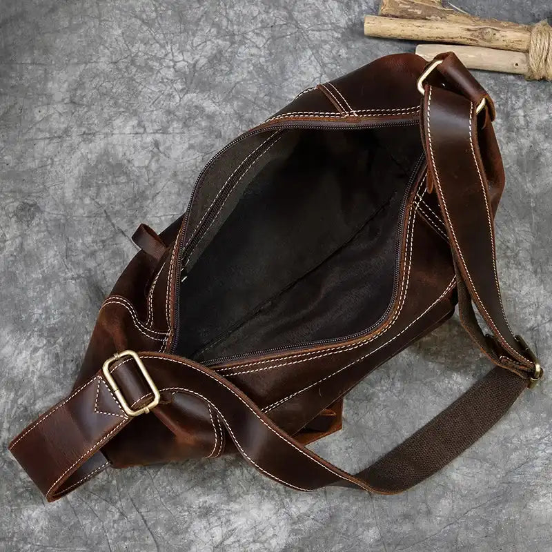 Open brown leather bag displaying its spacious interior and strap.