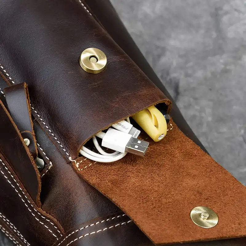 Close-up of a leather bag pocket containing charging cables and a USB drive.