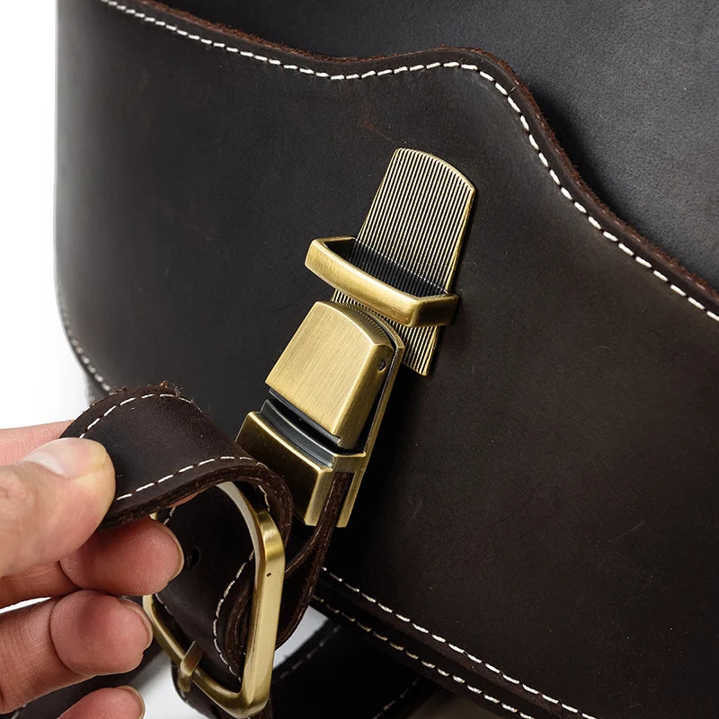 Close up of a dark brown leather bag, showing a gold metal buckle and white stitching,