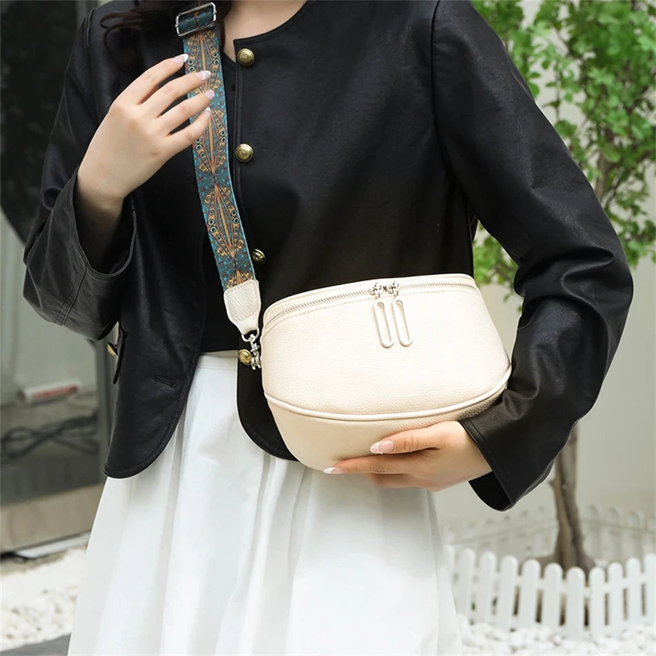 a woman holding a beige leather bag with patterned starp, wearing a black jacket and white skirt showcasing elegant look.