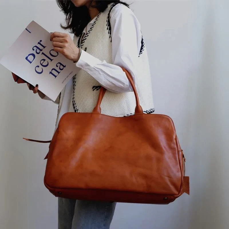 Woman holding a large brown leather handbag, wearing a vest and holding a magazine with the word Barcelona.