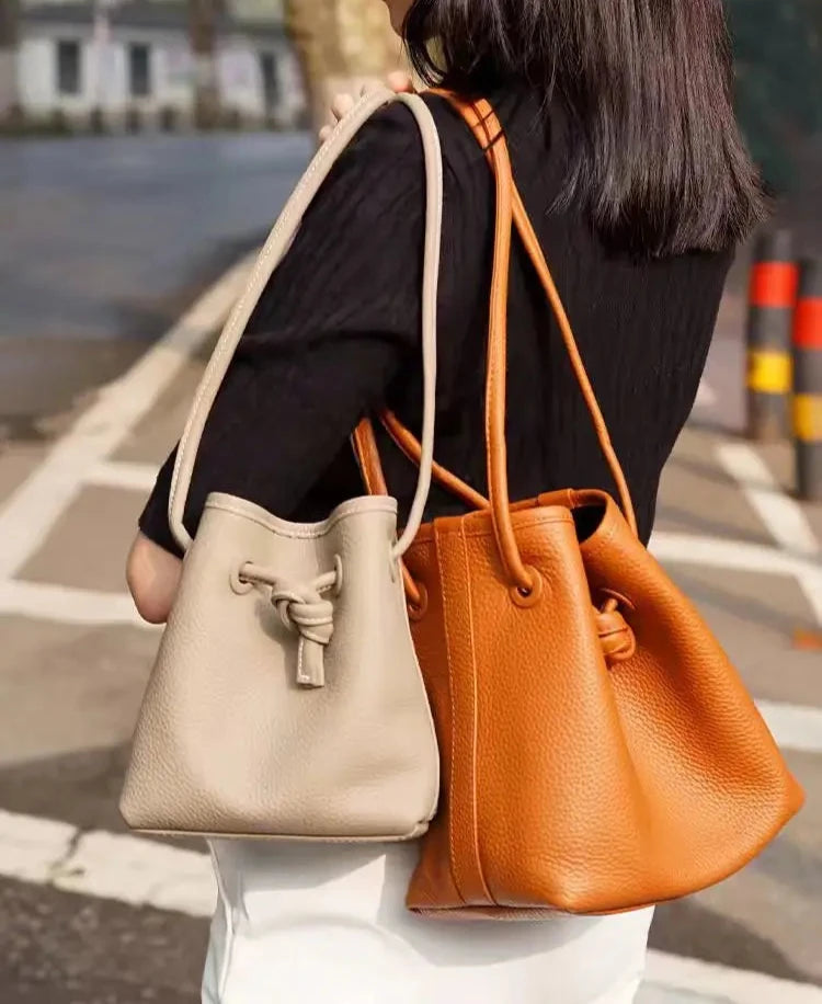 Woman carrying stylish white and brown leather bags in a city setting.