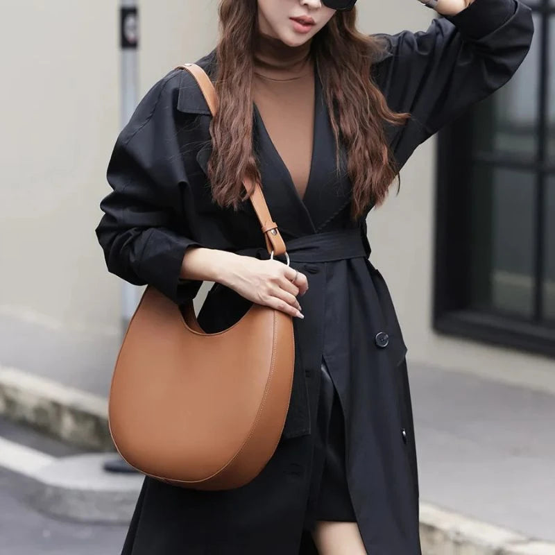model wearing an elegant brown leather bag, with a moon design and adjustable strap on her shoulder.