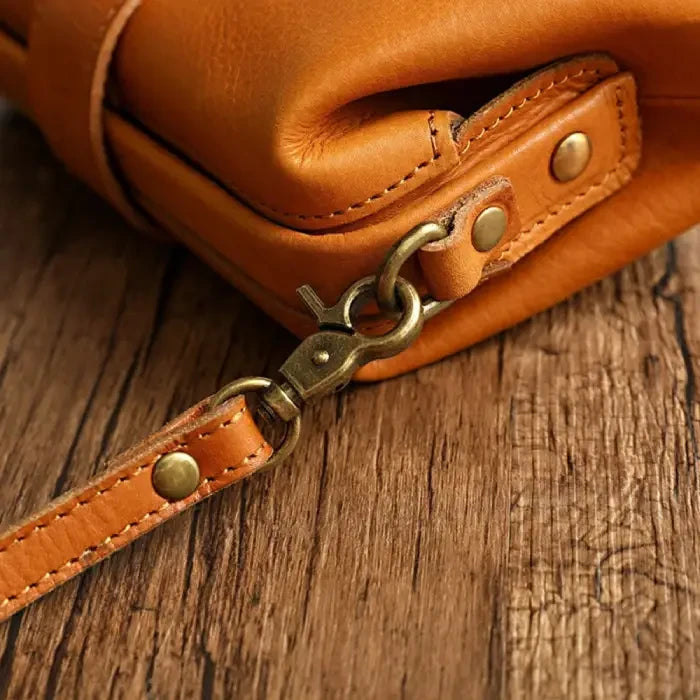 Close-up view of a brown leather bag with clasp and handle, highlighting the stitching and metal finish.