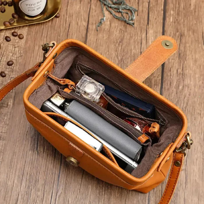 Brown leather bag with organized interior containing items such as cell phone, notebook and makeup.
