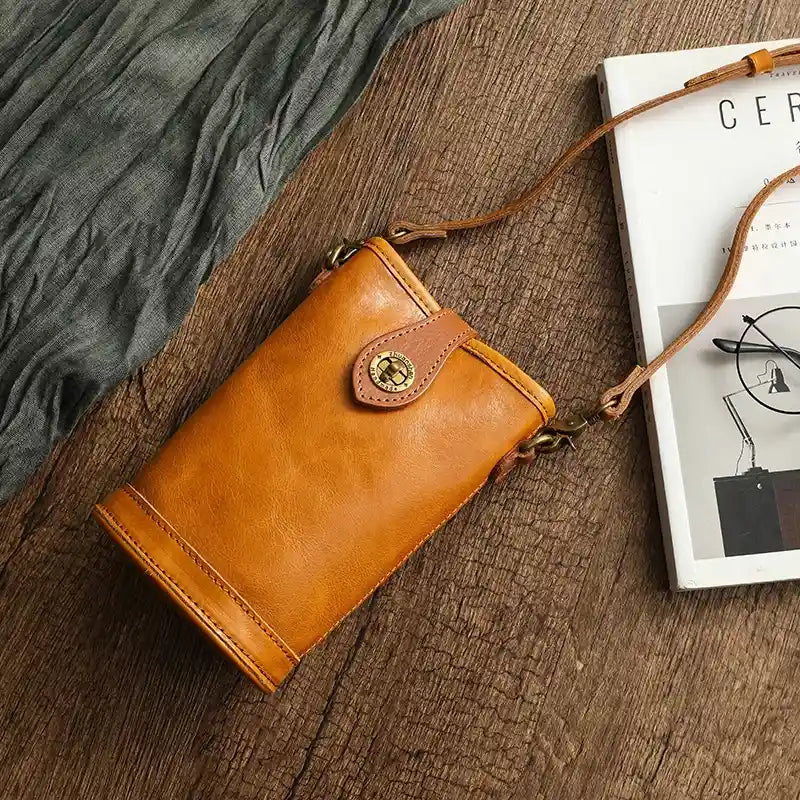 Chic brown leather crossbody bag with gold accents on a rustic background.