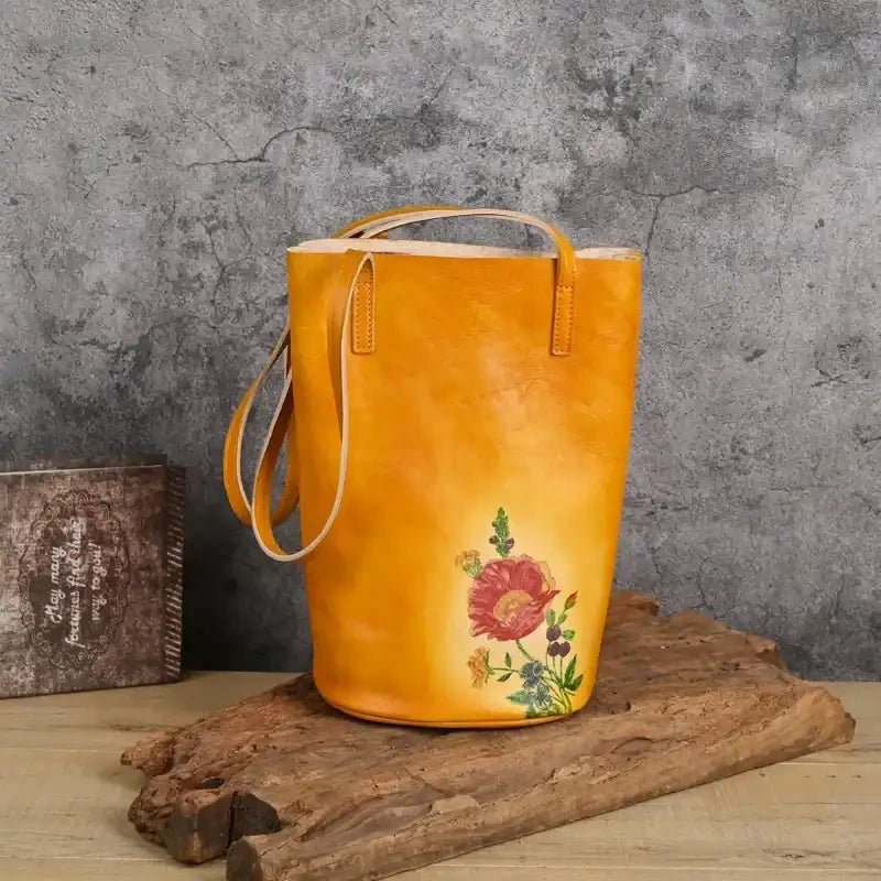Yellow leather tote bag with colorful floral print on a natural background, front view.